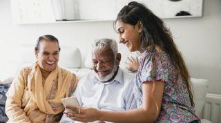 Young person smiling showing smiling older couple their mobile phone